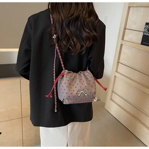 Detail of grey fabric bucket bag with red heart pattern and silver bow on model