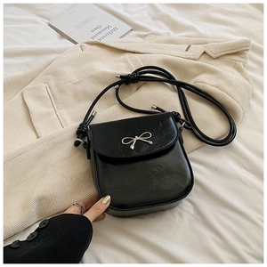 Minimalist black PU leather crossbody bag with golden bow decoration on white bedding