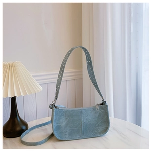 Sac bandoulière bleu clair en suédine avec bandoulière à œillets sur marbre blanc