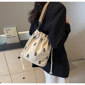 Détail du sac seau en toile beige avec broderie dollar et cordon de serrage à franges