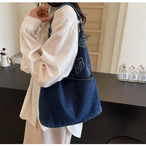 Détail de la broderie rose blanche sur un sac fourre-tout en denim bleu foncé texturé