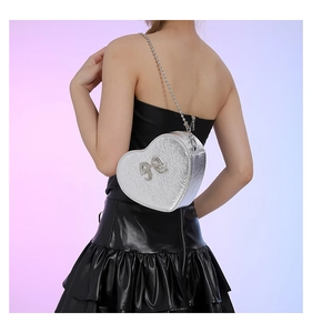 Model wearing a heart-shaped silver PU crossbody bag with rhinestone bow detail