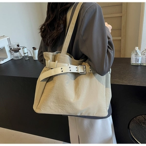 Close-up of beige tote bag with white leather belt detail in a modern café setting