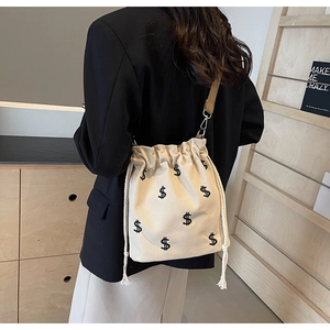 Détail du sac seau en toile beige avec broderies de signes dollar et fermeture à cordon