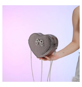 Detail of silver heart-shaped crossbody bag with rhinestone bow and beaded chain
