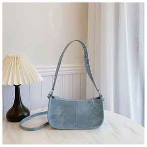 Gros plan du sac baguette en daim bleu clair avec garniture argentée sur marbre