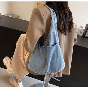 Détail de la broderie de rose sur un sac hobo en jean bleu clair porté par un mannequin