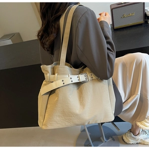 Beige oversized tote bag with decorative belt detail shown in a stylish home setting