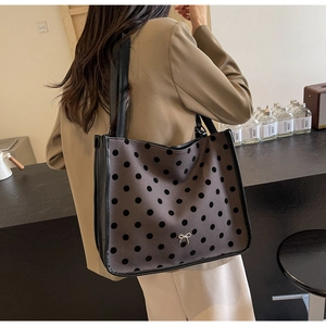 Detailed back view of a dark brown polka dot tote bag with a metal bow and long handles