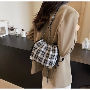 Detail of checkered drawstring bucket bag with metal bow accessory and chain strap