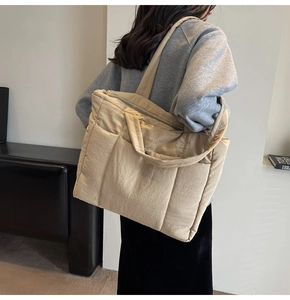 Detail of beige quilted tote bag showing padded fabric texture and zipper closure