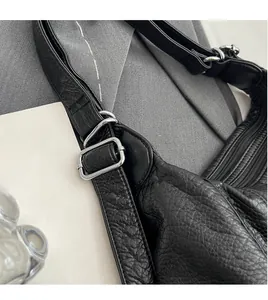 Detail view of adjustable strap with silver buckle on black litchi pattern leather bag