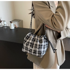 Detail of checkered canvas bucket bag with silver bow pendant and chain strap