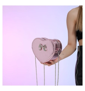 Detail of pink heart-shaped crossbody bag with rhinestone bow and silver bead chain strap