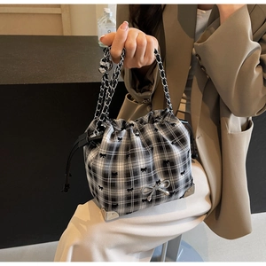 Detail of checkered crossbody bucket bag with black bows and silver corner protectors