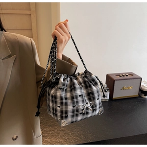 Detail of black and white checkered tweed bucket bag with silver bow hardware and chain strap