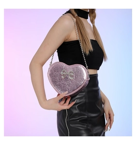 Close-up of pink heart-shaped crossbody bag with metallic texture and silver bow detail