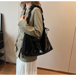 Detail of black glossy faux leather hobo bag featuring ruffled shoulder strap and silver logo