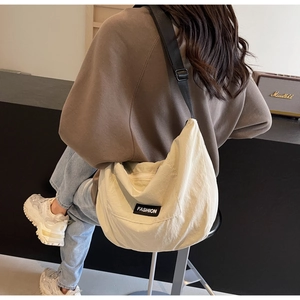 Detailed view of cream nylon crescent crossbody bag with black wide strap on model