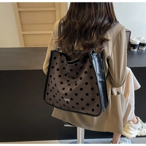 Detailed back view of a grey polka dot tote bag with leather trim and bow on model