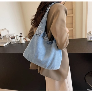 Détail de la broderie de rose blanche et fermeture à bouton sur le sac cabas en denim
