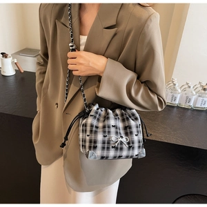 Detail of checkered bucket bag with silver bow and woven chain strap on a model