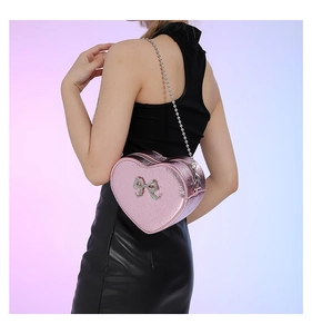 Detail of a pink heart-shaped crossbody bag featuring a sparkling sequin bow and chain strap