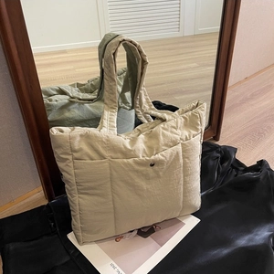 Fashionable beige quilted tote bag with padded handles and front pocket on leather background