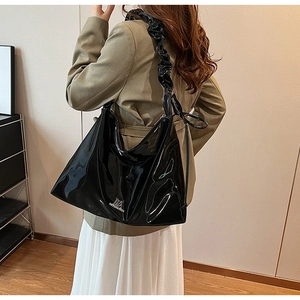 Detail of glossy black PU leather tote bag with wide pleated strap and silver metal logo