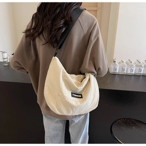 Detail of a cream fabric crescent crossbody bag featuring a black fashion label and wide strap