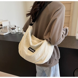 Detail of a cream crescent crossbody bag with adjustable strap worn by a model