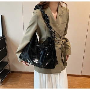 Detail of black glossy PU leather handbag featuring unique ruffled shoulder straps and logo