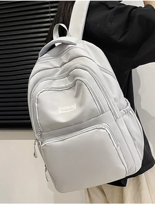 Detail view of light grey nylon backpack showing multiple zipper compartments and side pocket