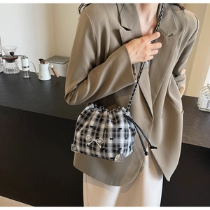 Close-up of black and white checkered crossbody bag with silver bow detail and chain strap