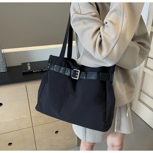 Detail of black fabric tote bag featuring decorative belt with metal eyelets and silver buckle