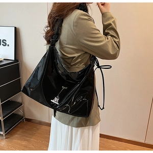 Detail of glossy black PU shoulder bag featuring metallic logo and drawstring strap