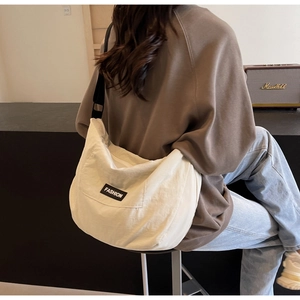 Detail view of a cream canvas crescent crossbody bag with a black fashion label on the front