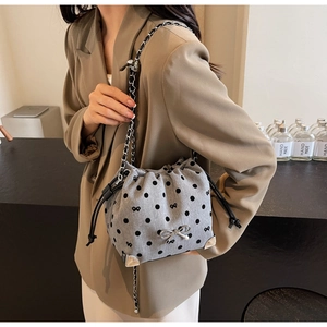 Detail of grey polka dot bucket bag featuring silver bow charm and metal chain strap