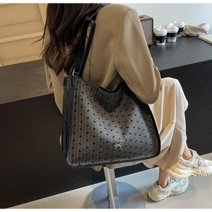 Close-up of a black tote bag with bow patterns and metal logo in a cafe setting