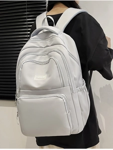 Detail view of a light grey nylon backpack with multiple zipper pockets and fashion label