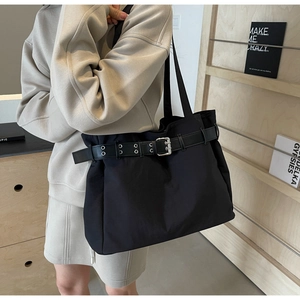 Detail of a large black nylon tote bag with silver eyelet belt accents on a female model
