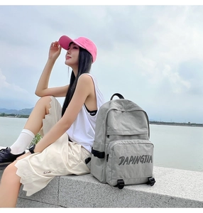Outdoor shot of a grey nylon backpack with front zipper pocket and logo by a lake