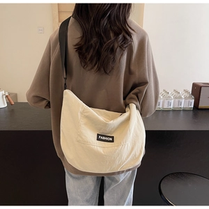 Detail view of cream canvas crossbody bag with wide black strap on a model's back