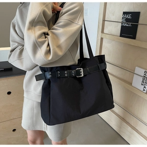 Detail of black nylon tote bag featuring a decorative leather strap with silver buckle
