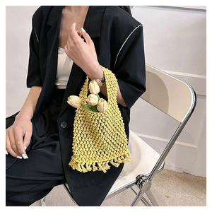 Detail of yellow woven tote bag featuring hollow mesh pattern and long fringe tassels