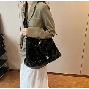 Close-up of a glossy black PU leather shoulder bag with metallic logo on a female model