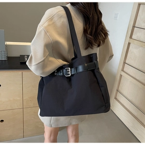 Detail of a large black nylon tote bag with decorative buckle belt and long shoulder strap