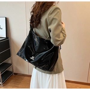 Polished black faux leather tote bag with silver logo detail worn by a model
