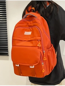 Détail d'un grand sac à dos orange en nylon avec plusieurs compartiments zippés
