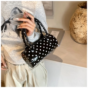Detail of a black cylinder bag with white polka dots and smooth patent leather surface